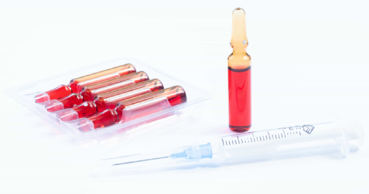 Five sealed vials of red liquid in a tray, with one open vial and a syringe, set on a sterile surface in a medical or lab setting for Vitamin Injections in Gig Harbor, WA.